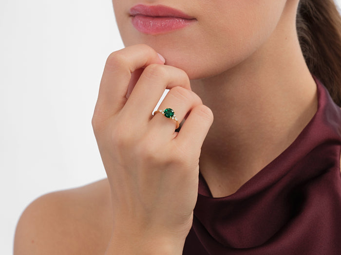 Round side cluster ring setting with marquise accents in yellow gold on the hand near the chin, green display stone