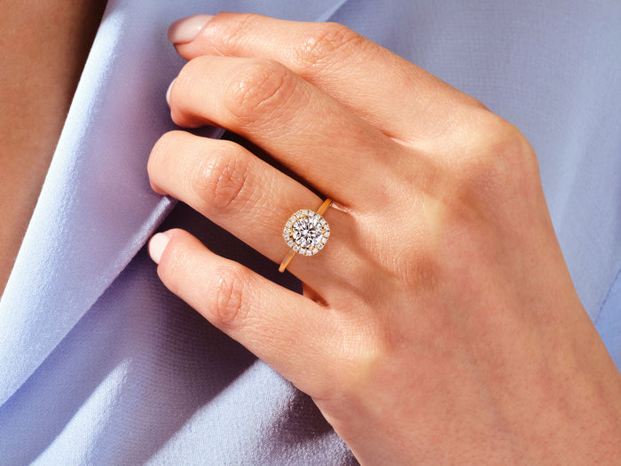 Round moissanite cushion halo ring in gold worn on the hand against a blue jacket