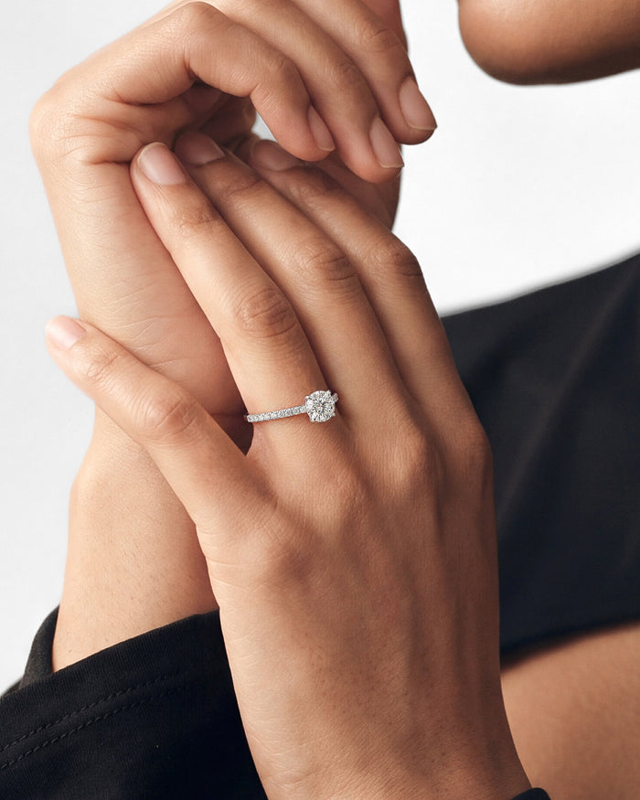 Round lab grown diamond pave engagement ring in white gold worn on the hand with fingers laced