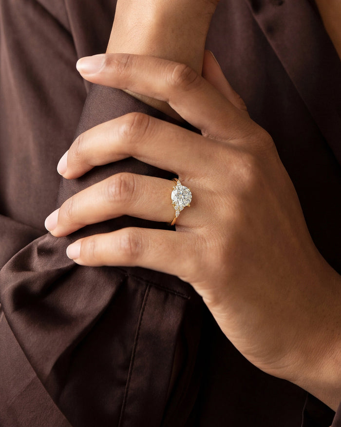 Round lab grown diamond vintage cluster ring worn on the hand gripping a brown satin sleeve