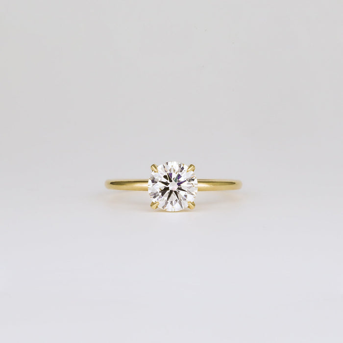 Round brilliant moissanite four claw solitaire engagement ring on a plain yellow gold band