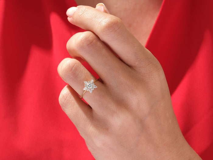 Round moissanite star halo engagement ring worn on the hand against a red background