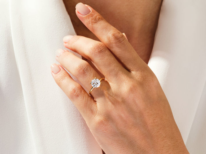 Round lab grown diamond four prong engagement ring with hidden halo worn on the hand in yellow gold