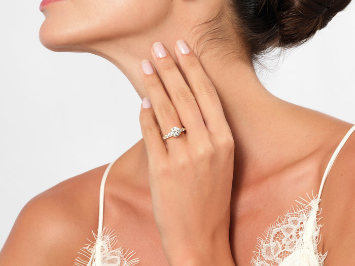 Round lab grown diamond side stone engagement ring in yellow gold worn on the hand at the collarbone