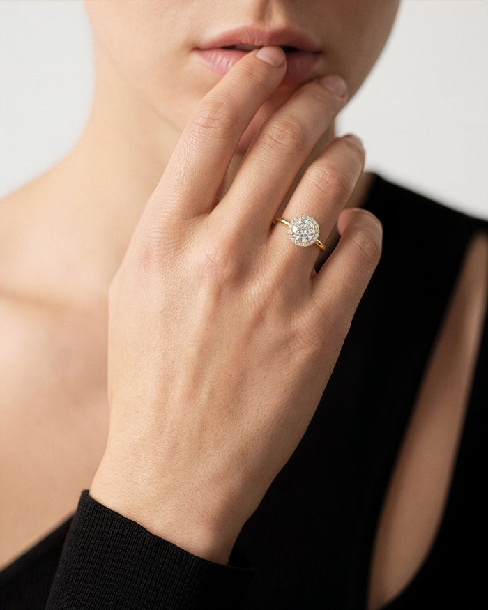 Round cut moissanite halo engagement ring in yellow gold worn on the hand near the lips