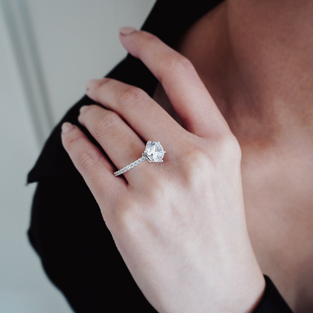 Round brilliant moissanite high basket engagement ring on a fine pave shank in white gold