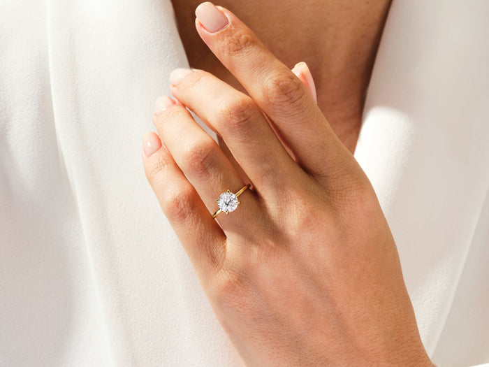 Round brilliant moissanite hidden halo ring in yellow gold worn on the ring finger