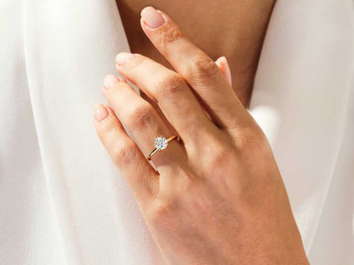 Dainty round moissanite hidden halo ring in yellow gold worn on the hand