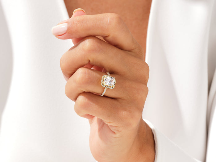 Radiant moissanite halo ring in gold worn on the hand, fingers curled toward the palm