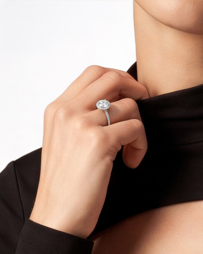 Round brilliant lab grown diamond halo ring in white gold on a hand holding a black collar
