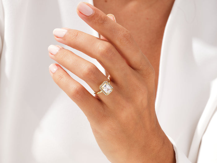 Radiant lab grown diamond halo engagement ring worn on the hand against a white blazer