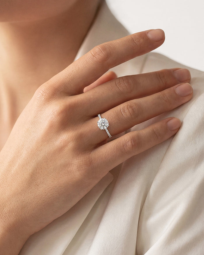 Round lab grown diamond micro pave ring in white gold worn on the hand resting on a cream blouse