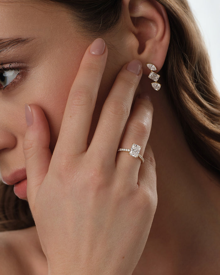 Elongated radiant lab grown diamond micro pave ring worn on the hand at the cheek beside drop earrings