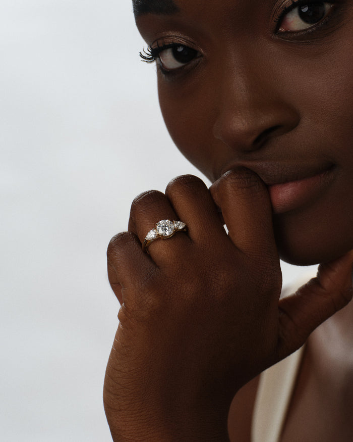 Round lab grown diamond ring with pear side stones worn on the hand held at the lips