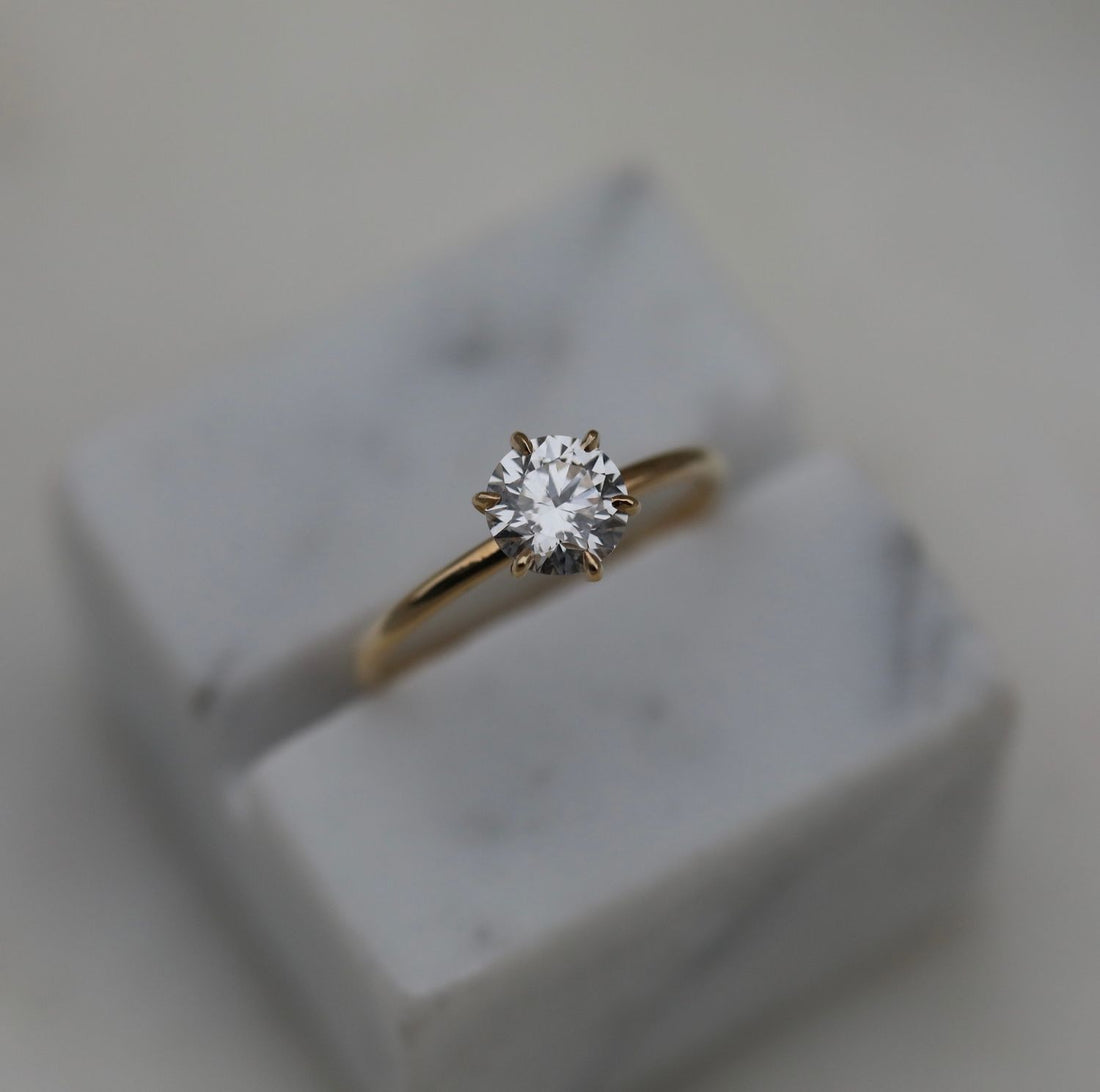 Round brilliant moissanite six claw solitaire engagement ring on a round wire yellow gold band