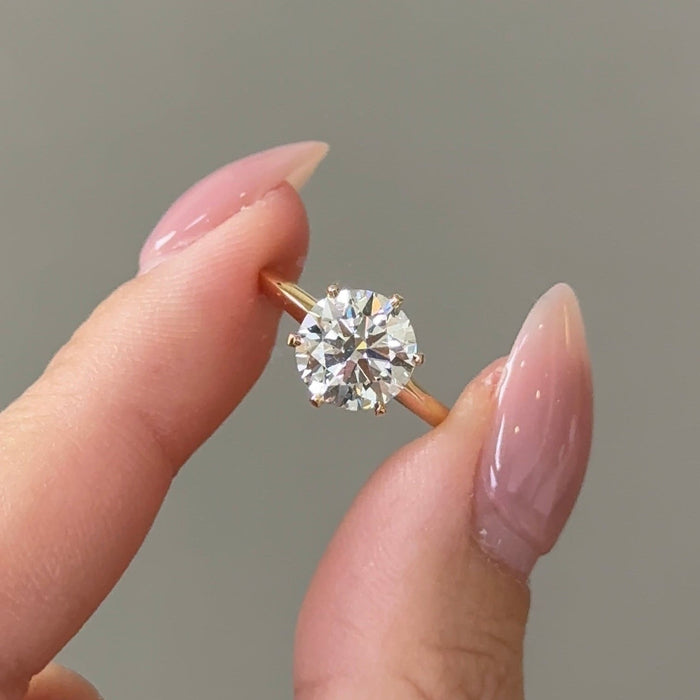 Round cut moissanite six claw solitaire engagement ring on a fine band in yellow gold