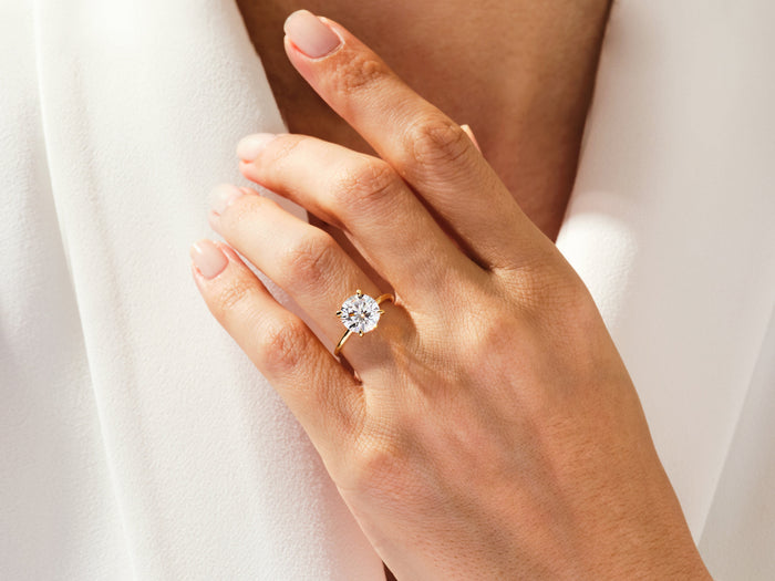 Large round lab grown diamond secret halo ring in yellow gold worn on the hand with fingers spread