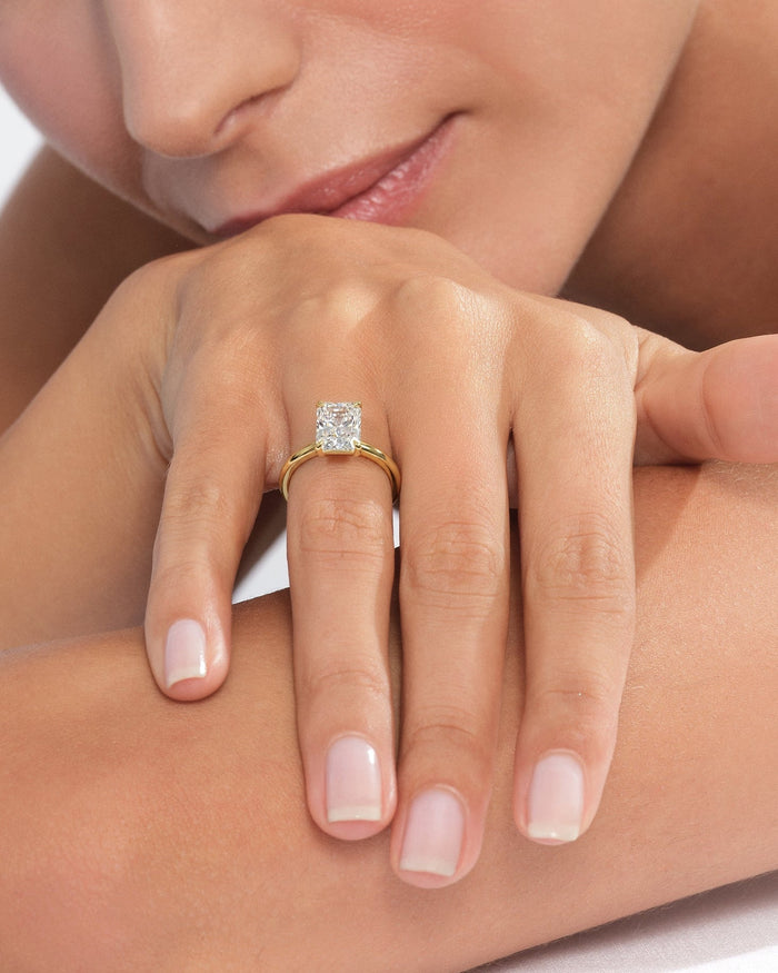 Radiant cut moissanite solitaire ring in yellow gold worn on the hand resting on the arm