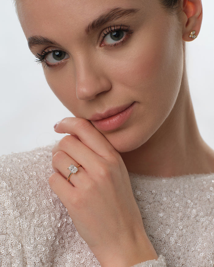 Radiant moissanite solitaire engagement ring in gold worn on the hand near the chin