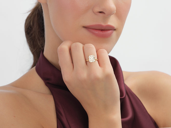 Large radiant moissanite solitaire engagement ring in gold worn on the hand at the chin
