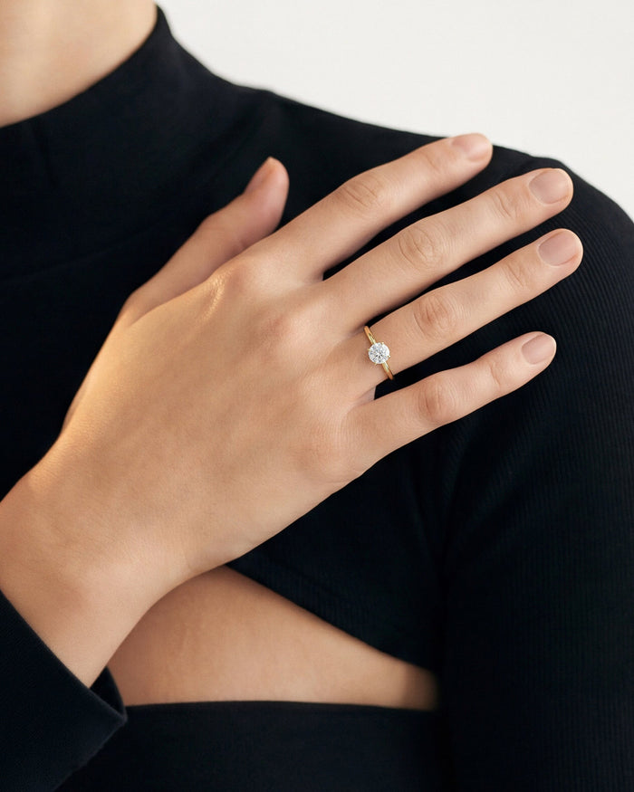 Round lab grown diamond classic solitaire in yellow gold worn on a hand resting on the shoulder of a black top