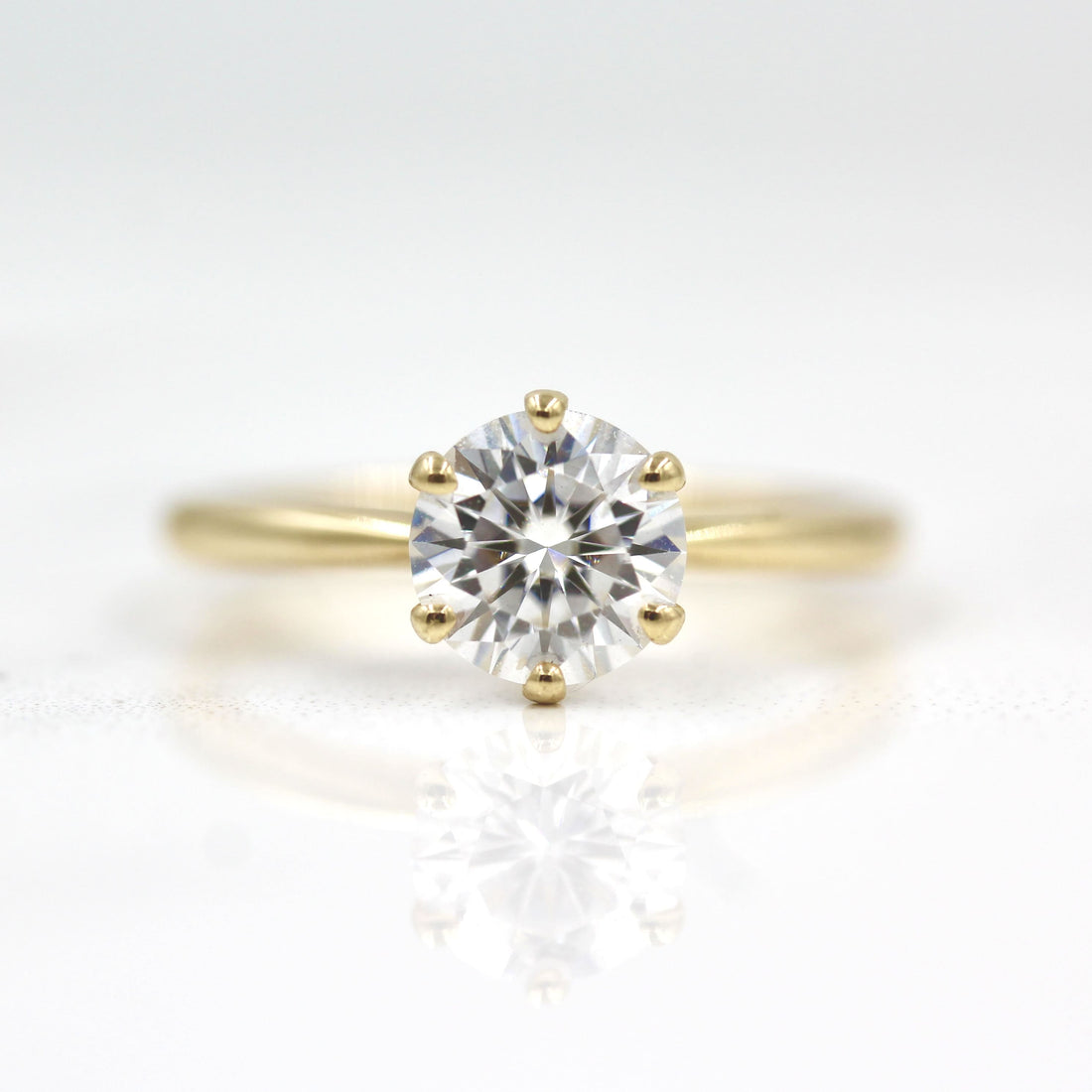 Round brilliant moissanite six claw solitaire engagement ring on a satin finished yellow gold band