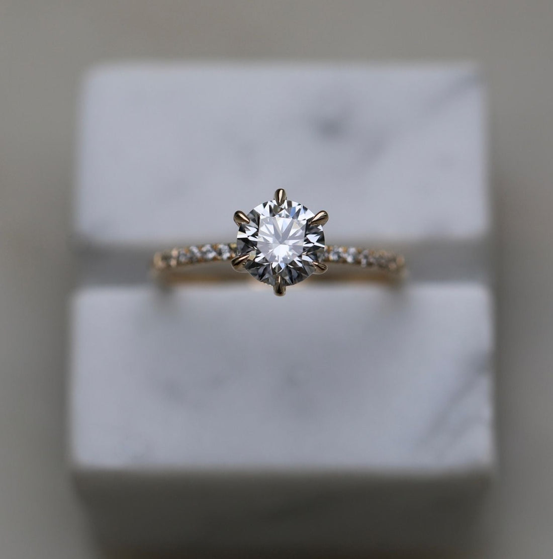 Round brilliant moissanite six tapered claw engagement ring on a French pave band in yellow gold