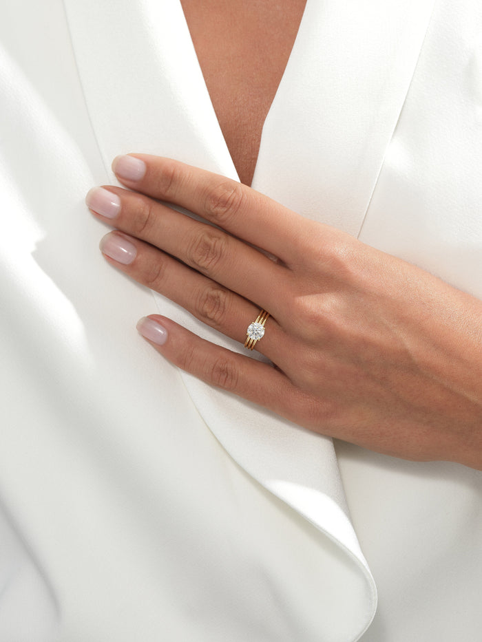 Round moissanite triple band engagement ring in yellow gold worn on the hand against a white jacket