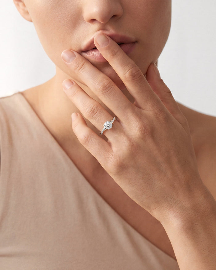 Round lab grown diamond twist engagement ring in white gold worn on the hand raised to the lips