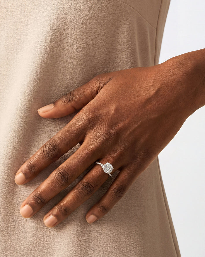 Round lab grown diamond crossover twist engagement ring in white gold worn on the hand against a beige dress