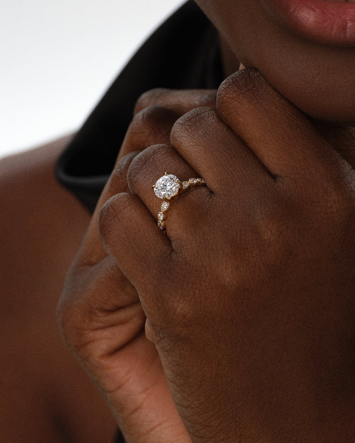 Round moissanite vintage milgrain ring in yellow gold worn on the hand near the chin