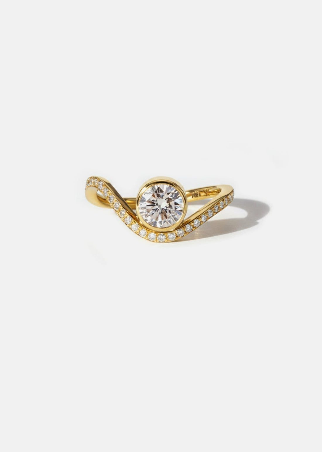 Round brilliant moissanite bezel set engagement ring on a pave wave band in yellow gold