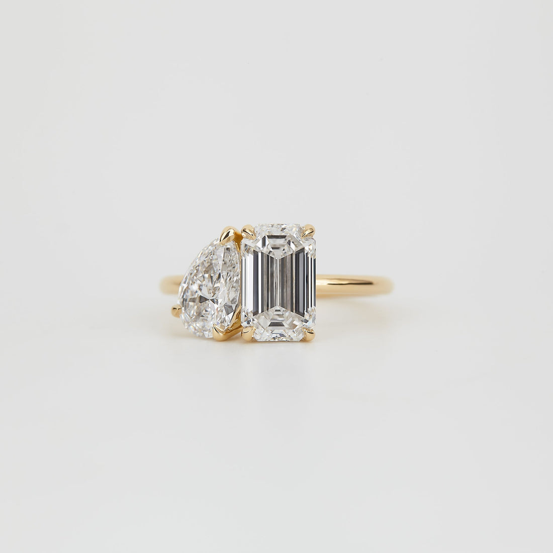 Emerald cut and pear moissanite toi et moi engagement ring on a fine yellow gold band