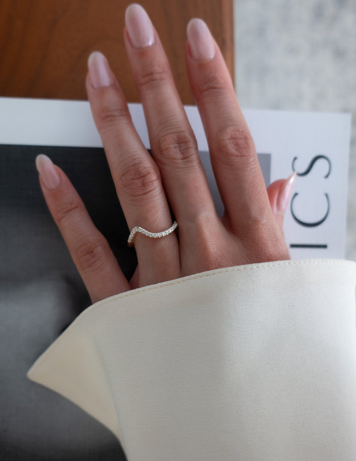 Curved wave pave wedding band with moissanite worn on a hand holding a magazine