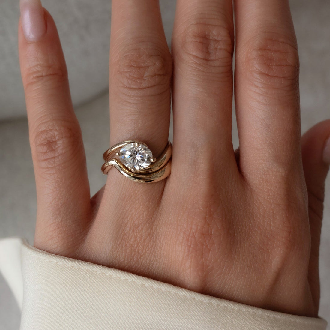 East-west oval lab grown diamond swirl bridal set with plain curved band in yellow gold on the hand