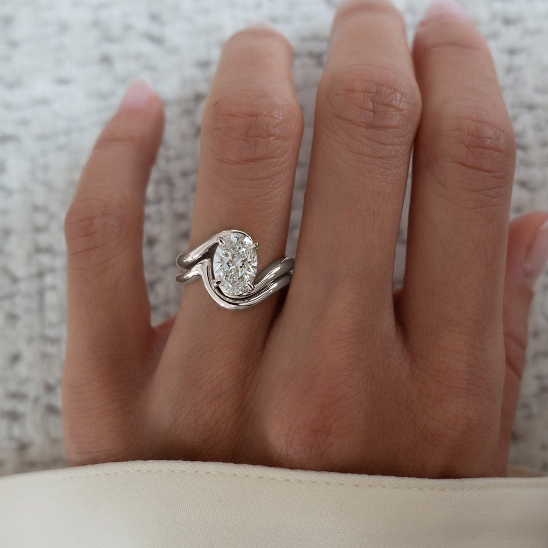 Oval lab grown diamond swirl bypass solitaire with plain S-curve band in white gold worn on the hand