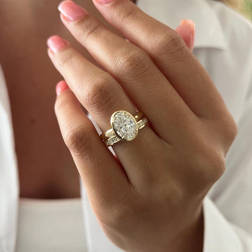 Oval moissanite claw bezel bridal set in yellow gold worn on the hand