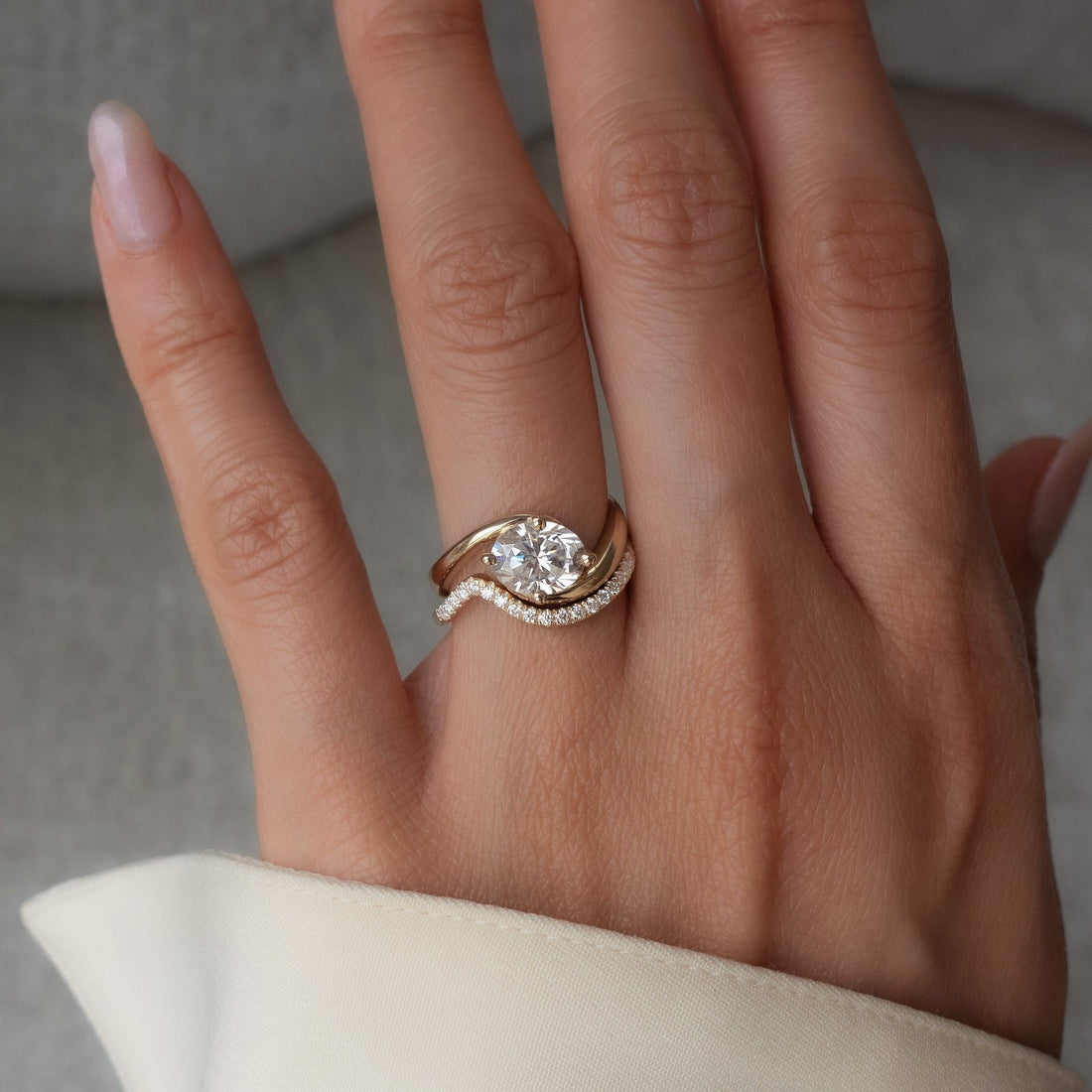East-west oval moissanite bypass bridal set with pave wave band in yellow gold worn on the hand