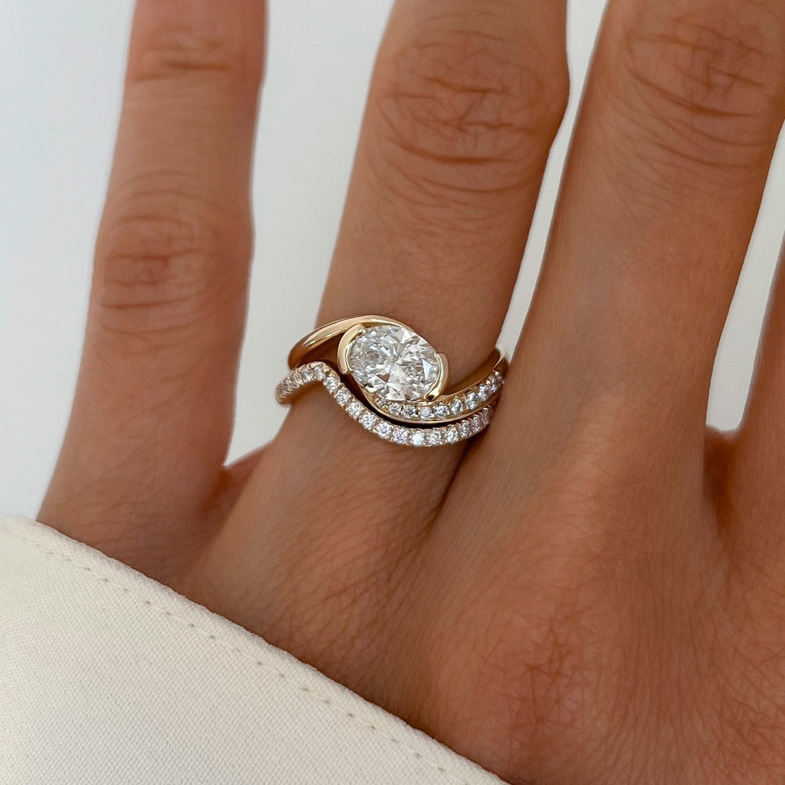 East-west oval moissanite half pave swirl ring with pave wave band in yellow gold on the hand