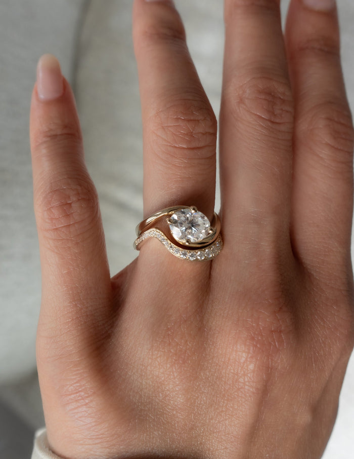 Oval moissanite bypass engagement ring with curved graduated stone band, top view on the hand