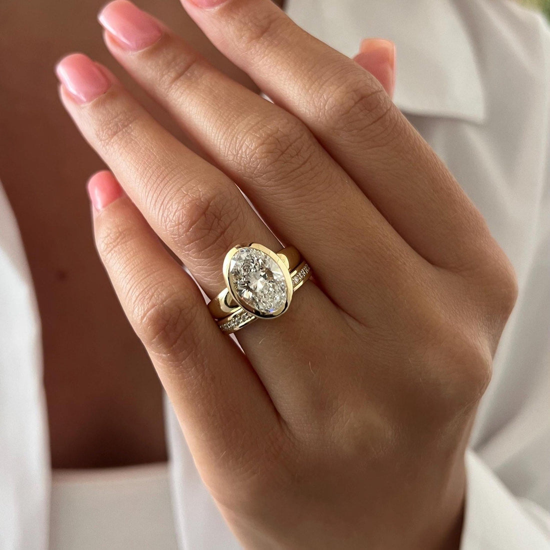 Oval moissanite full bezel bridal set with bold gold band worn on the hand