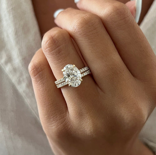 Oval moissanite hidden halo bridal set with half pave band in yellow gold worn on the hand