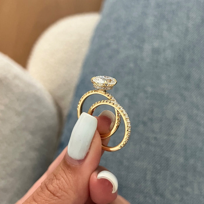 Oval moissanite engagement ring and pave wedding band held in the fingers showing the hidden halo