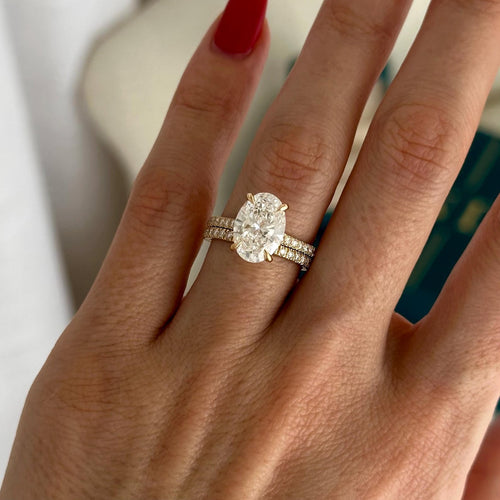 Oval moissanite hidden halo bridal set with matching pave band in yellow gold worn on the hand