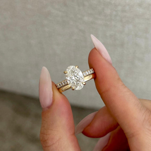 Oval moissanite hidden halo pave ring with plain yellow gold band held between the fingers