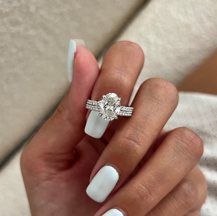 Oval moissanite pave engagement ring and straight pave band held between the fingers