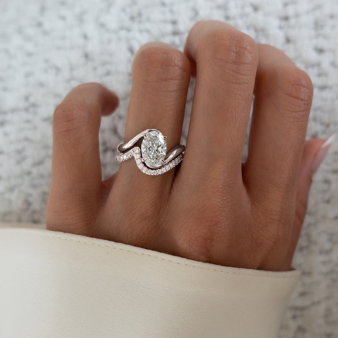 Oval moissanite swirl bypass solitaire with S-curve pave band in white gold worn on the hand
