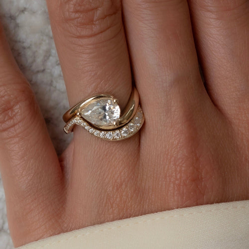 East-west pear lab grown diamond swirl bridal set with graduated pave wave band in yellow gold on the hand