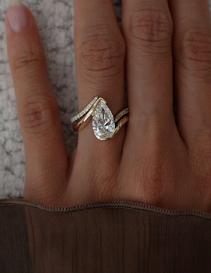 Close-up of north-south pear lab grown diamond bypass ring with peaked pave band above it