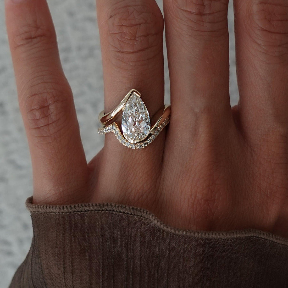 Pear lab grown diamond swirl bridal set with U-shaped pave band in yellow gold worn on the hand